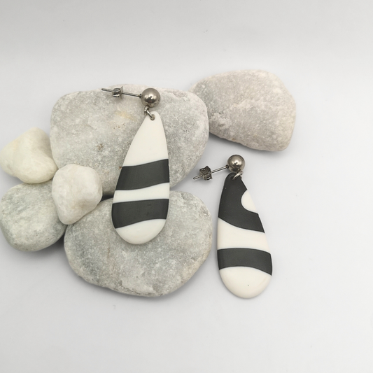Black and white striped polymer clay earrings on a white background with pebbles.
