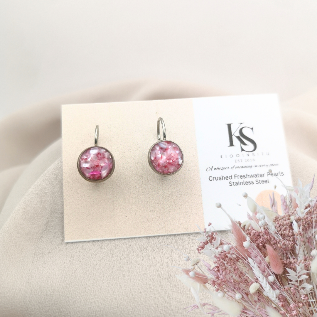 Handmade with care, these 8 mm stainless steel leverback earrings feature crushed freshwater pearls in soft pink hues, sealed beneath a clear, glass-like resin. 
