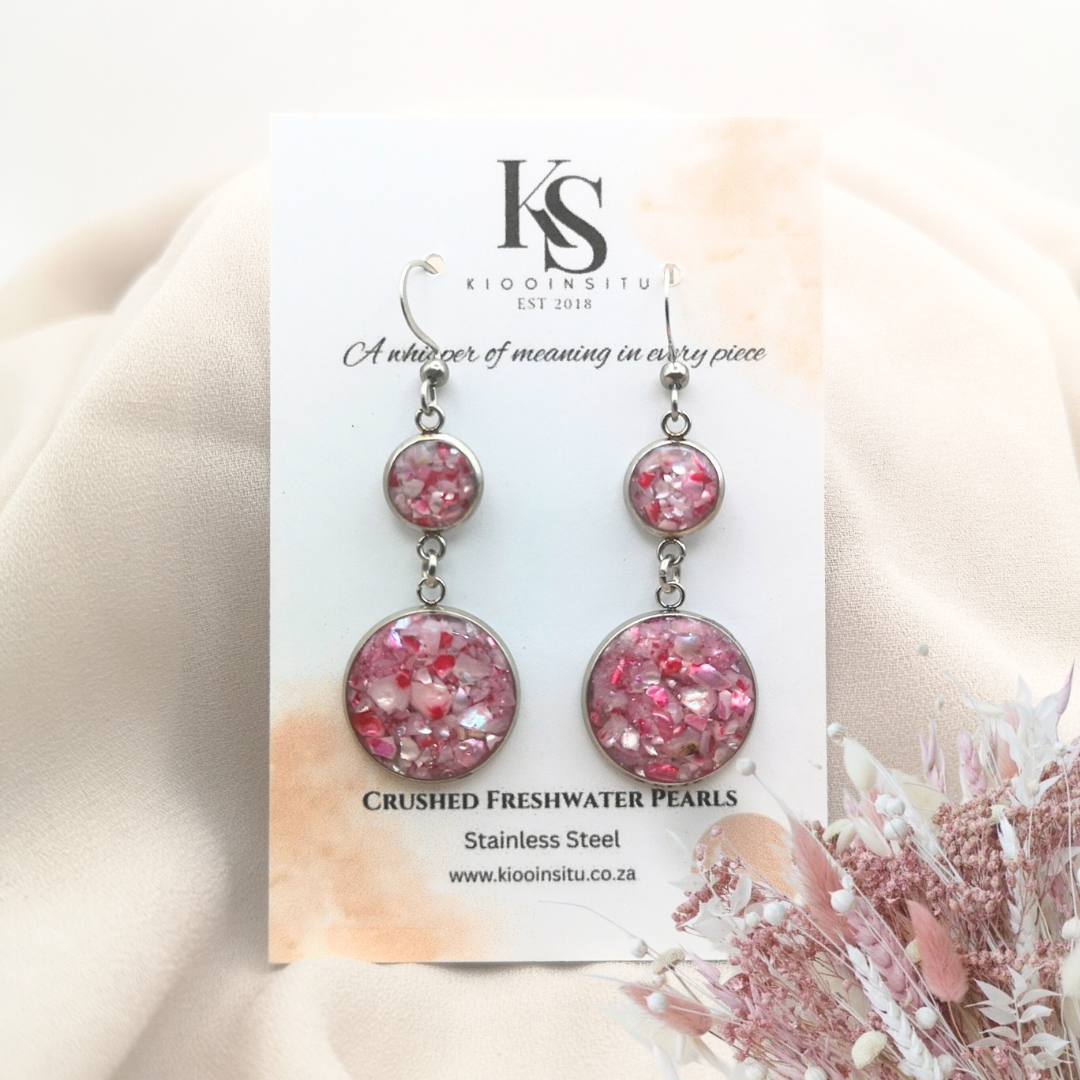 Crushed freshwater pearls in pink tones shimmer within 8 mm and 16 mm stainless steel bezels, sealed beneath a clear, glass-like resin that captures every glint of light.