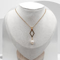 Gold necklace with a diamond-shaped pendant and pearl on a white mannequin bust.
