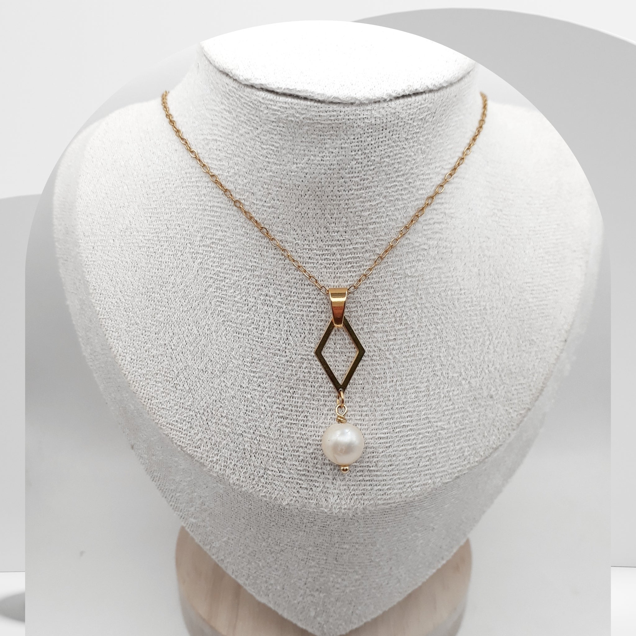 Gold necklace with a diamond-shaped pendant and pearl on a white mannequin bust.