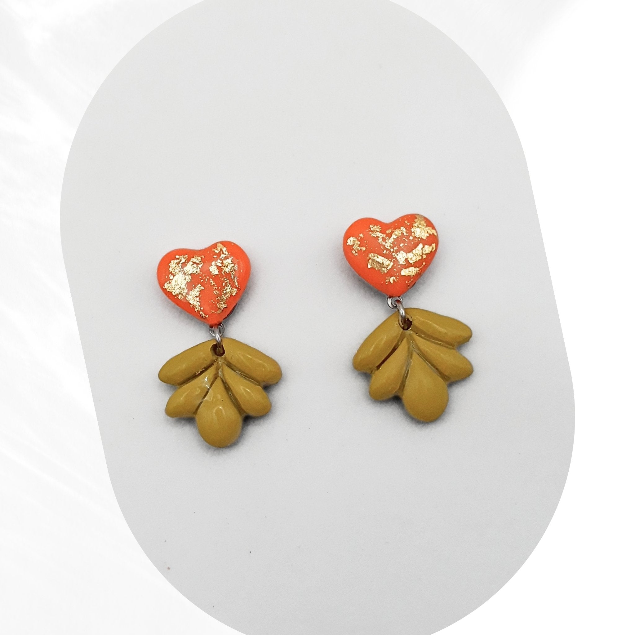 Heart-shaped orange earrings with gold accents and green leaf-like drops on a white background