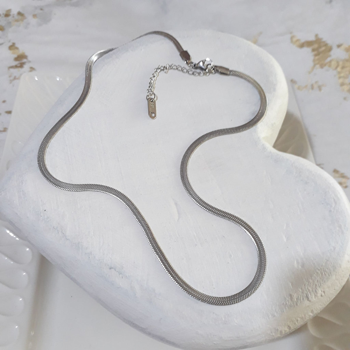 Herringbone silver stainless steel necklace lying on a white wooden heart