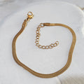 Herringbone gold-plated stainless steel bracelet lying on a wooden white surface