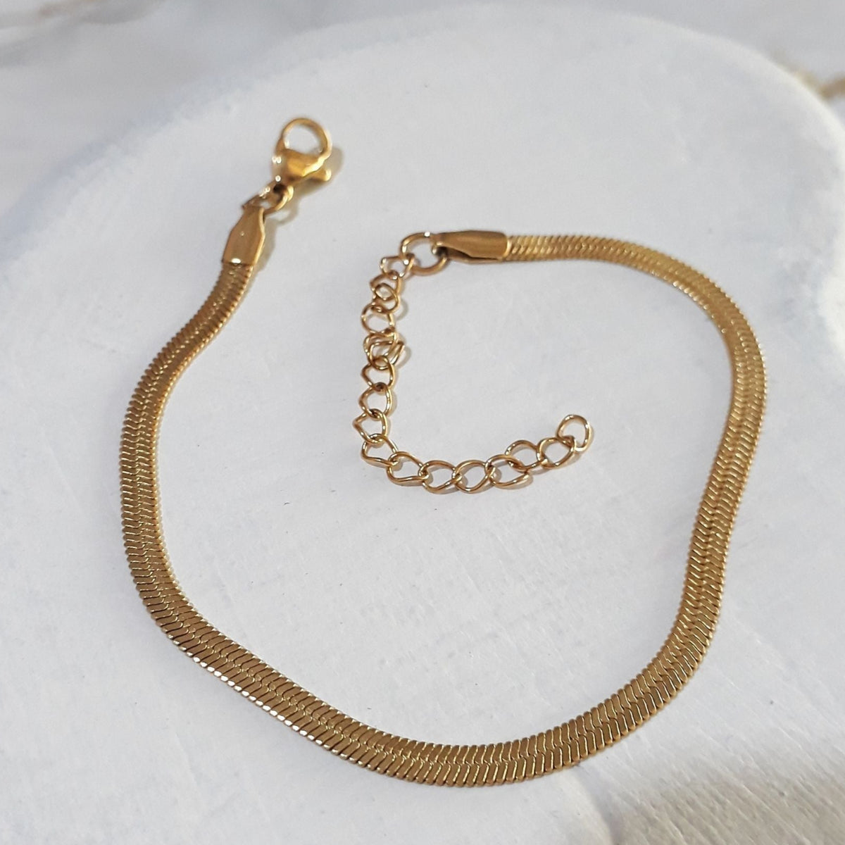 Herringbone gold-plated stainless steel bracelet lying on a wooden white surface