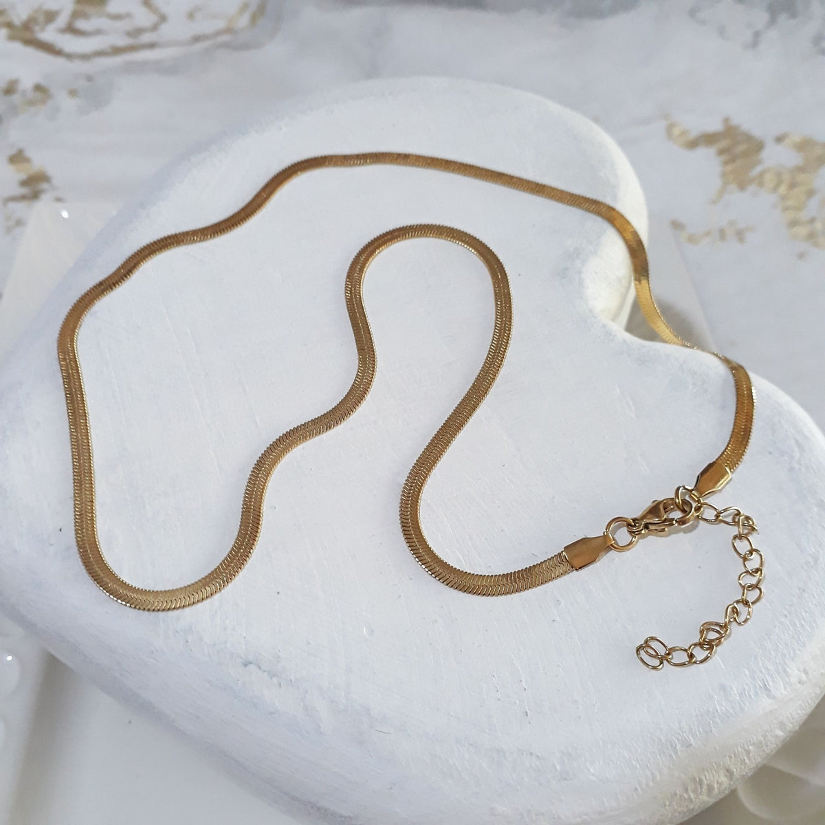 Herringbone gold-plated stainless steel necklace lying on a white wooden heart