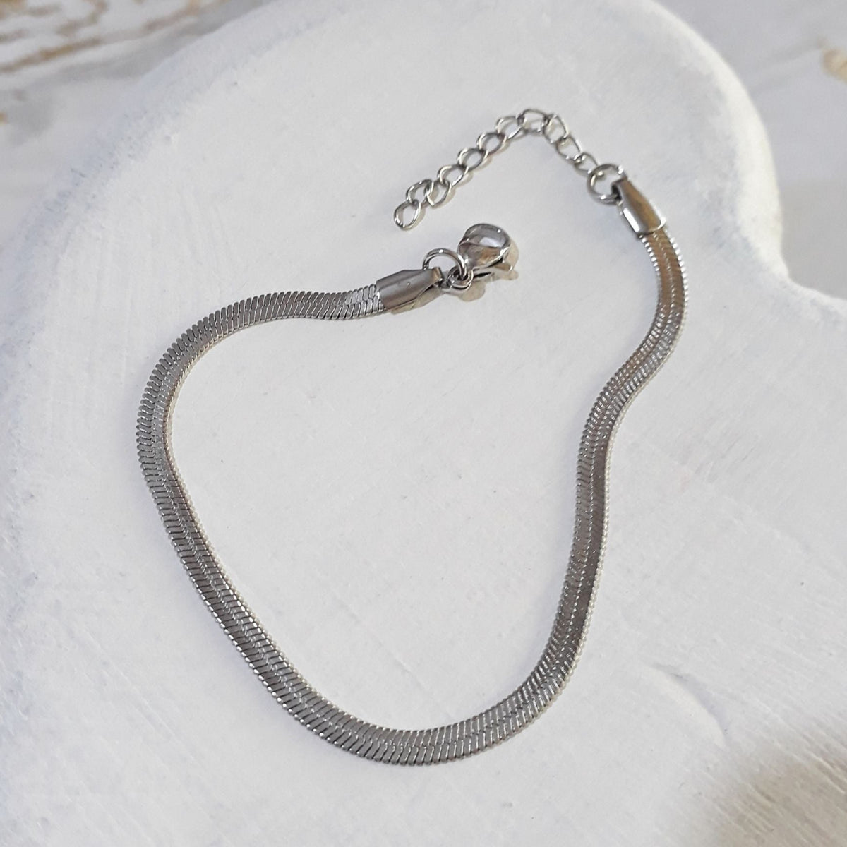 Herringbone silver stainless steel bracelet lying on a white wooden surface