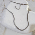 Herringbone silver stainless steel necklace lying on a white wooden heart
