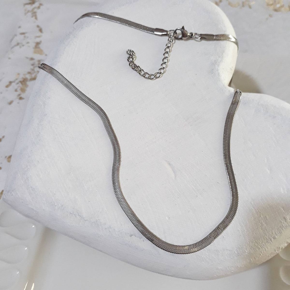 Herringbone silver stainless steel necklace lying on a white wooden heart