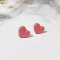 Pair of light pink heart-shaped polymer clay stud earrings with smooth, gently shiny surfaces.