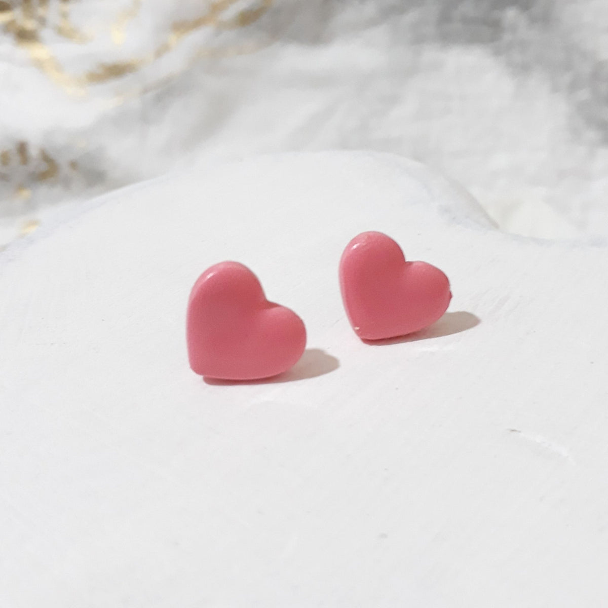 Pair of light pink heart-shaped polymer clay stud earrings with smooth, gently shiny surfaces.