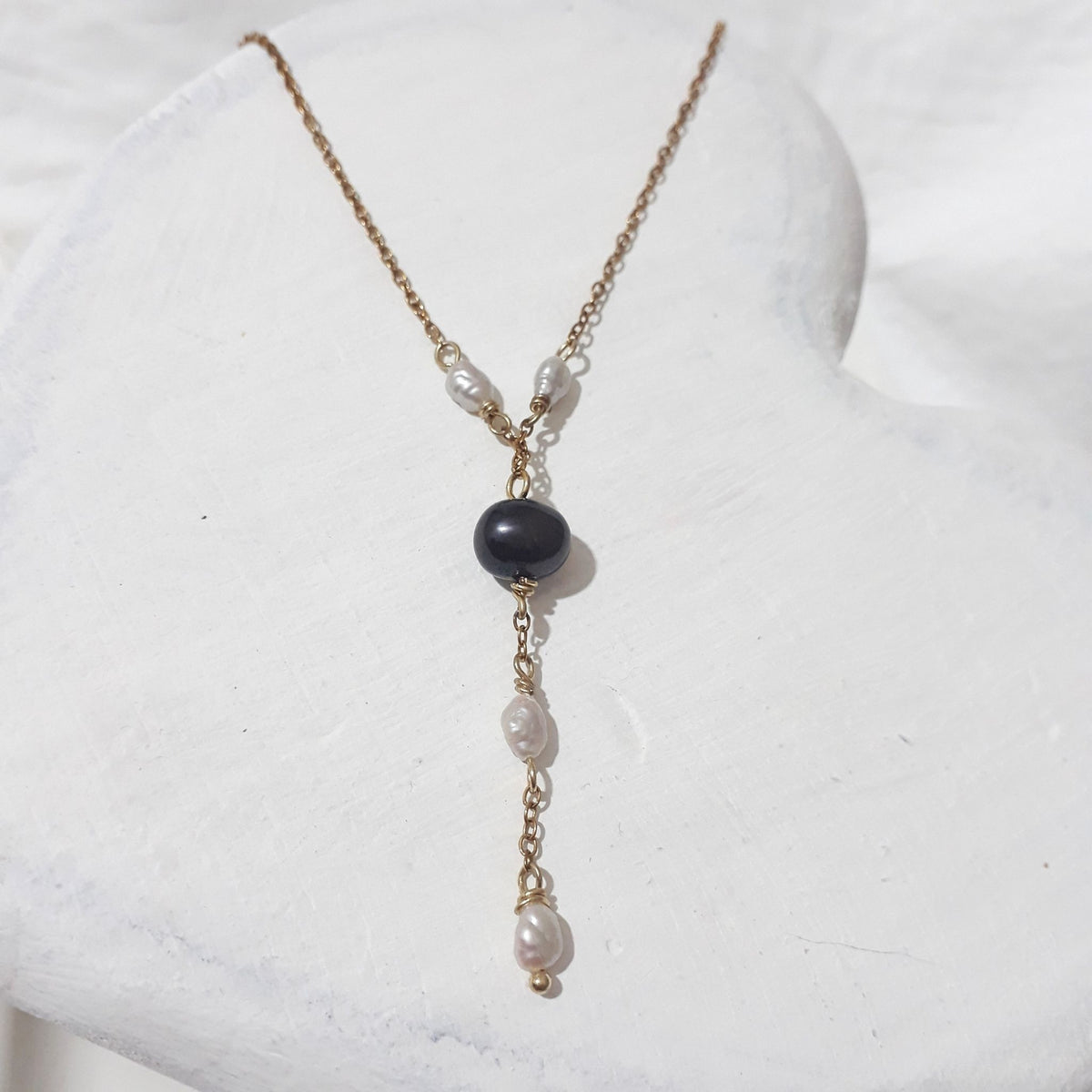 Midnight Blue Freshwater Pearl Y Necklace lying on a white wooden surgface