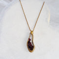 Red garnets sealed in clear resin inside an irregular gold-tone teardrop pendant on a gold-plated stainless steel chain.