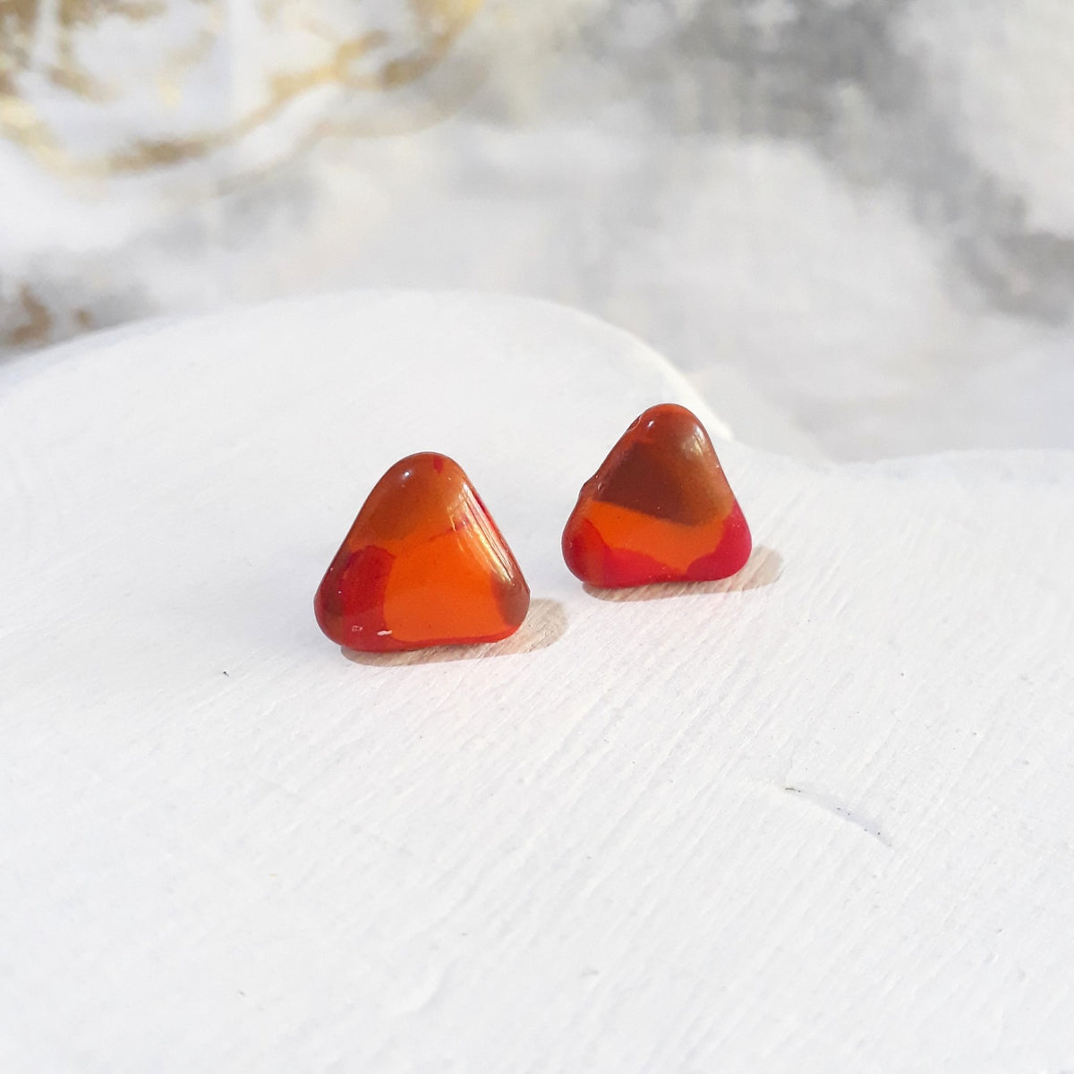 Glossy rounded triangle polymer clay stud earrings with orange, warm brown and deep red colour patches.
