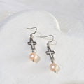 Soft peach freshwater pearls suspended beneath open silver-tone crosses on stainless steel ear hooks.