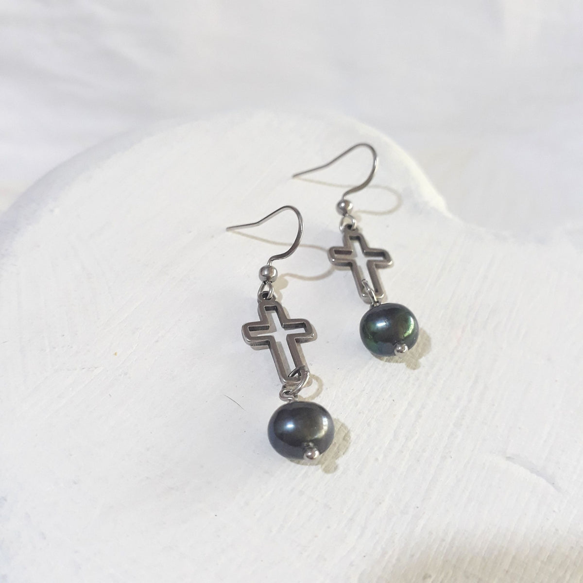 Dark peacock freshwater pearls suspended beneath open silver-tone crosses on stainless steel ear hooks.