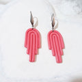 Glossy pink polymer clay drop earrings with curved arch lines, stepped ends and elongated silver-tone ear hooks.