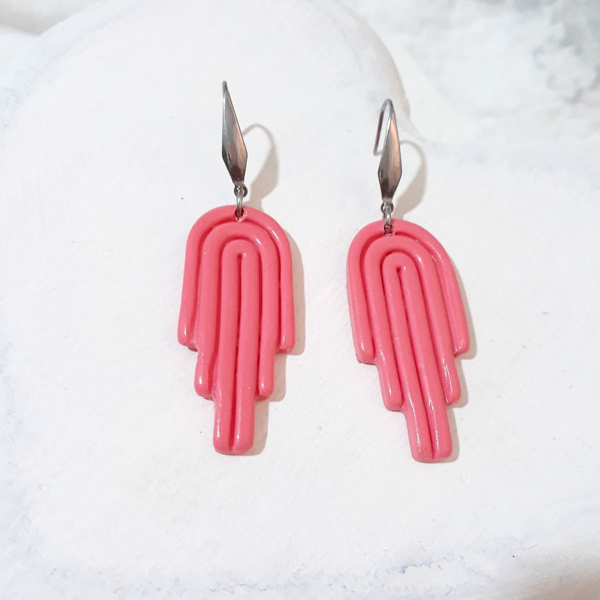 Glossy pink polymer clay drop earrings with curved arch lines, stepped ends and elongated silver-tone ear hooks.