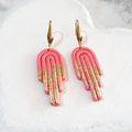 Glossy pink stepped arch polymer clay earrings with gold-coloured accents across the lower drops and elongated gold-tone ear hooks.