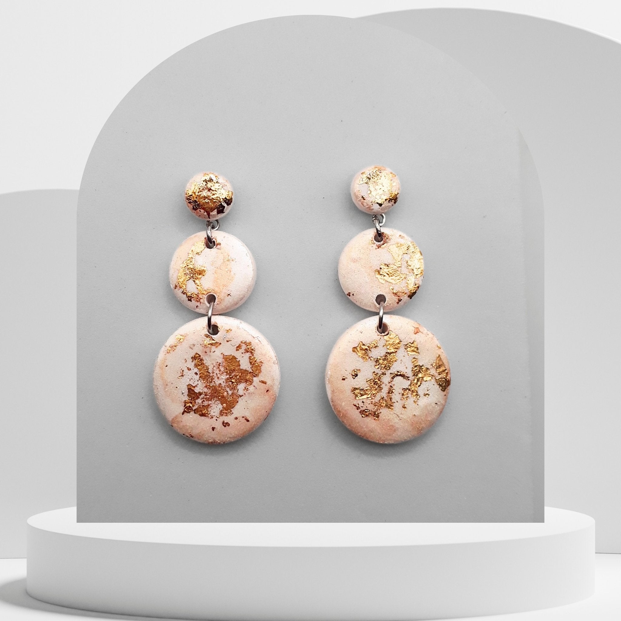 Pair of earrings with gold and pinkstone design on a gray background