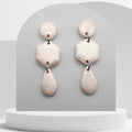 Pair of earrings with beige pearl-like polymer clay on a gray background