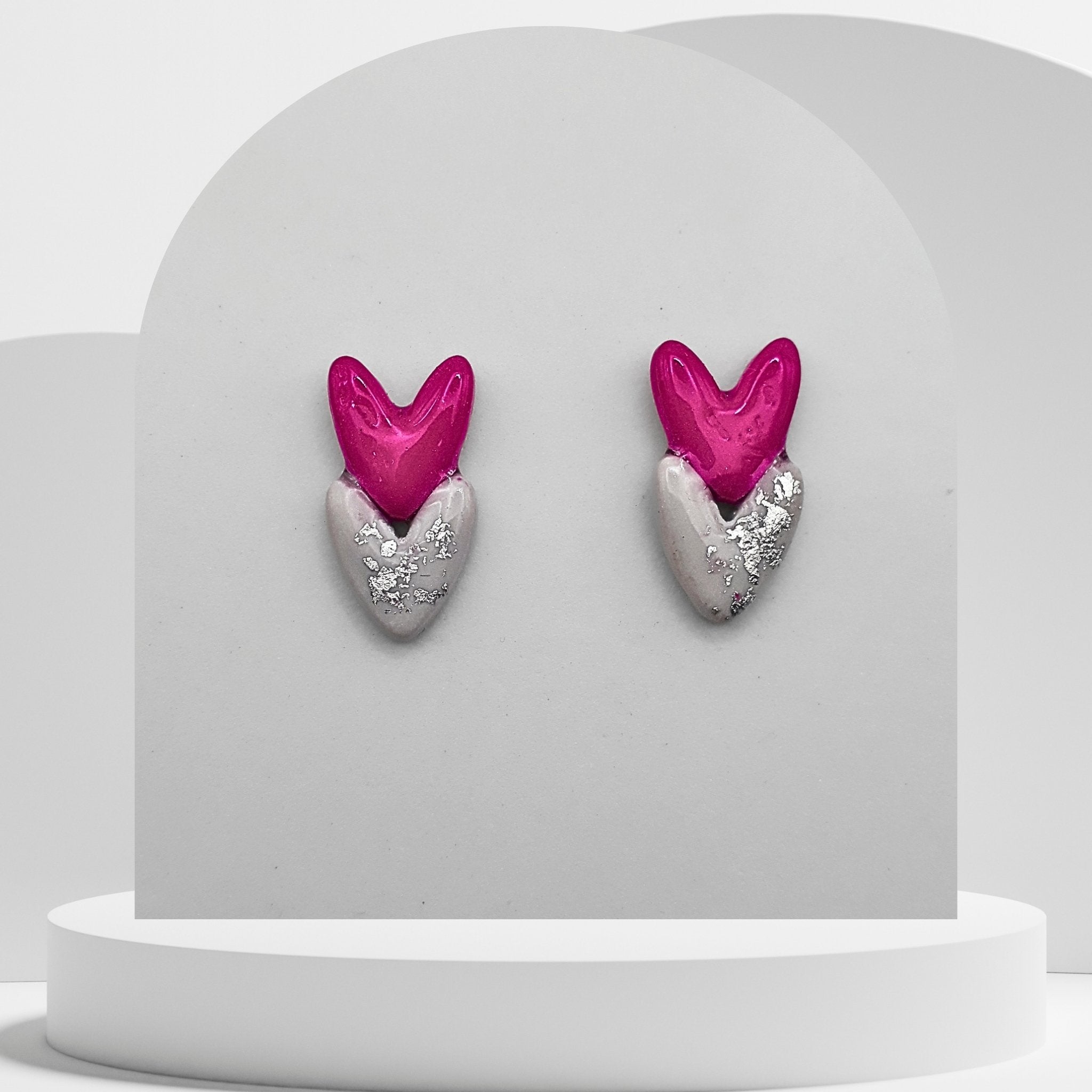 Heart-shaped earrings with pink hearts and silver bases on a gray stand.