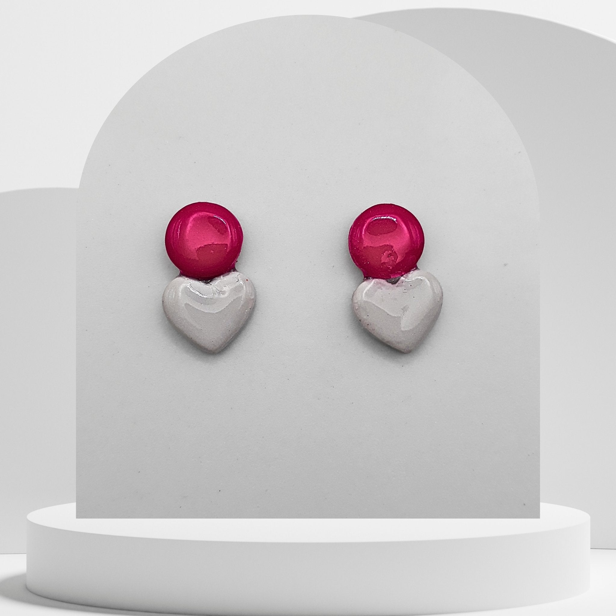 Heart-shaped earrings with red top and silver bottom on a white stand.