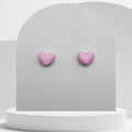 Pink heart-shaped earrings on a gray stand with a white background