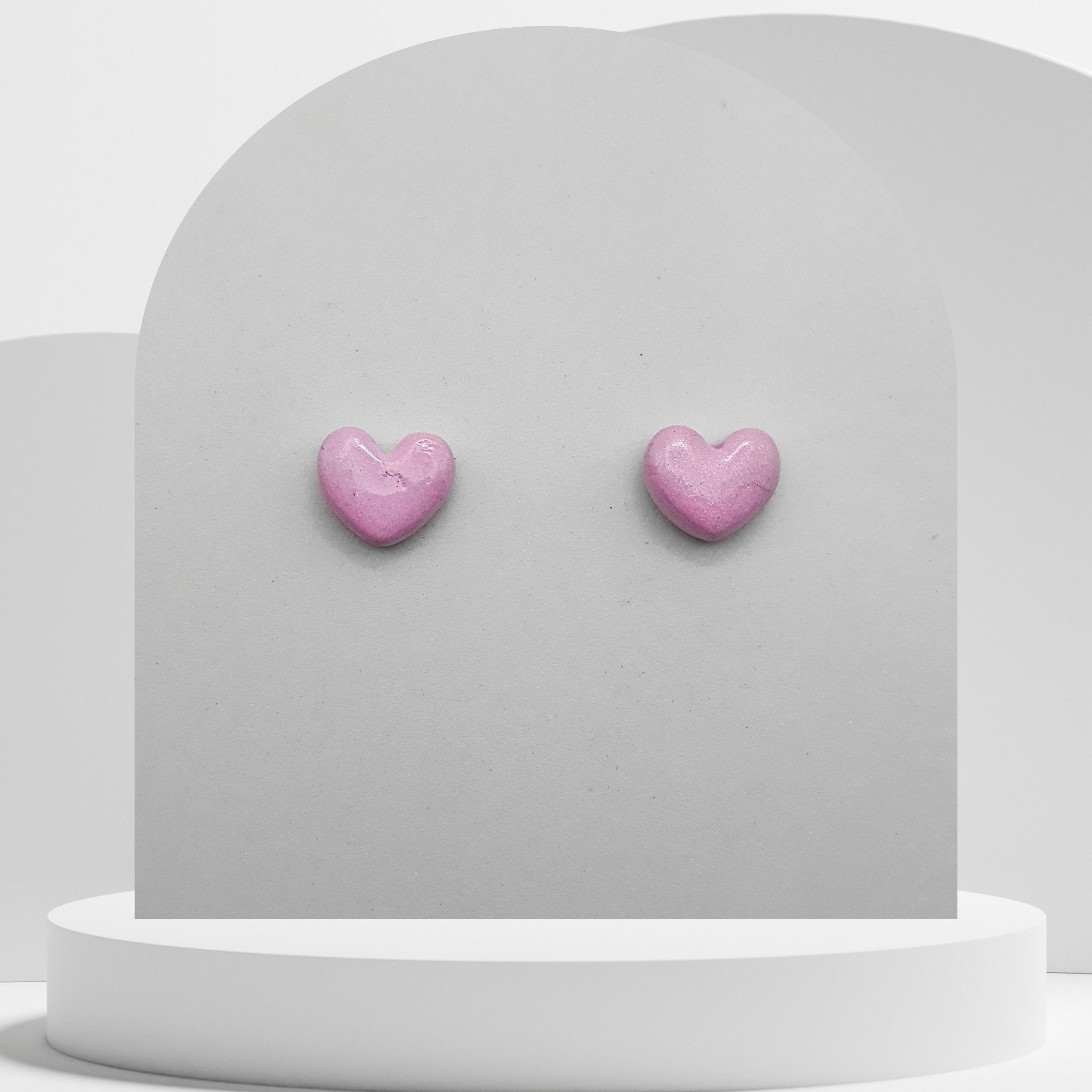 Pink heart-shaped earrings on a gray stand with a white background