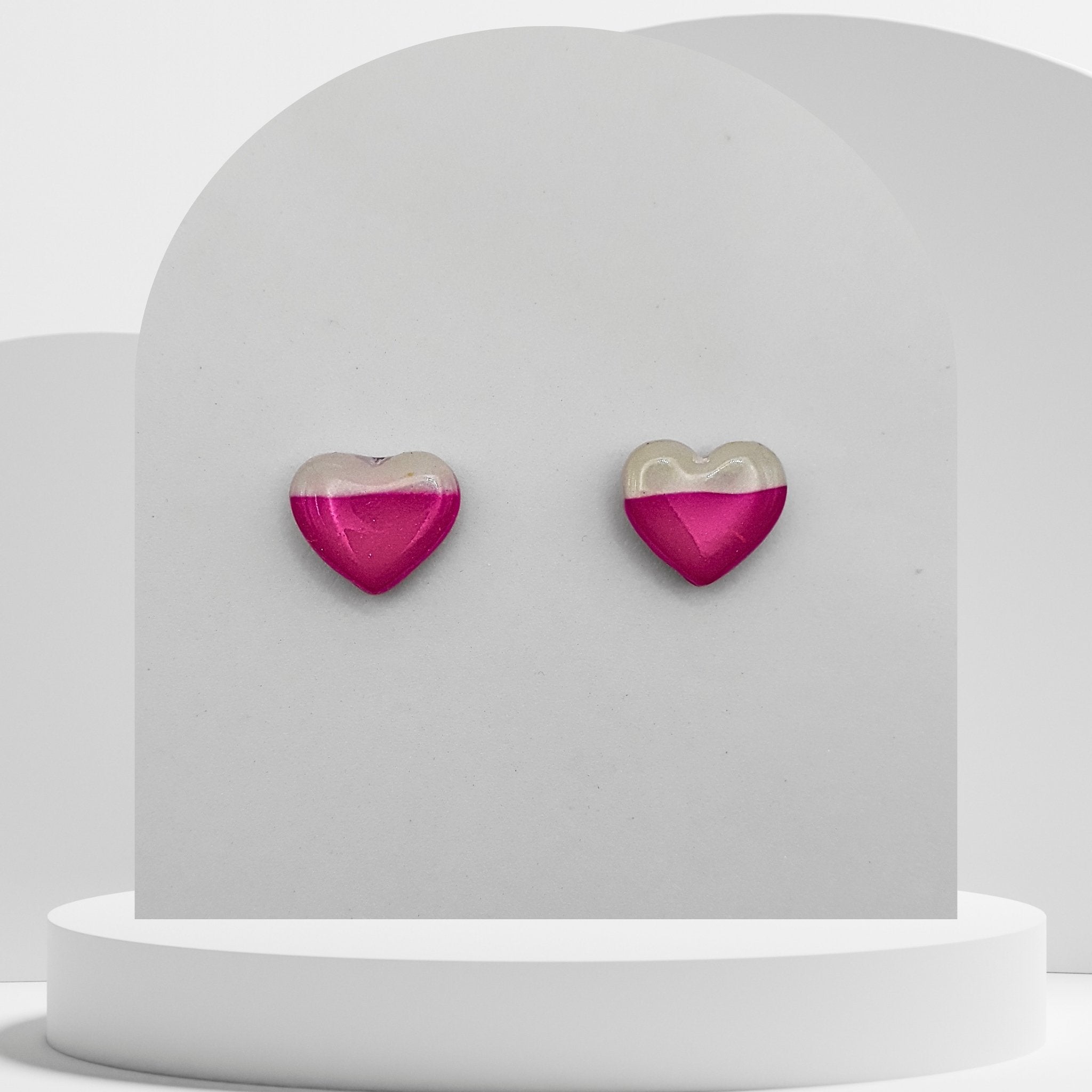 Heart-shaped earrings with pink and gold design on a white stand