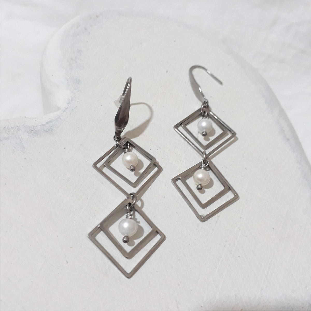 Stainless steel dangle earrings with two vertically linked sets of nested diamond-shaped frames, each holding a white freshwater pearl.