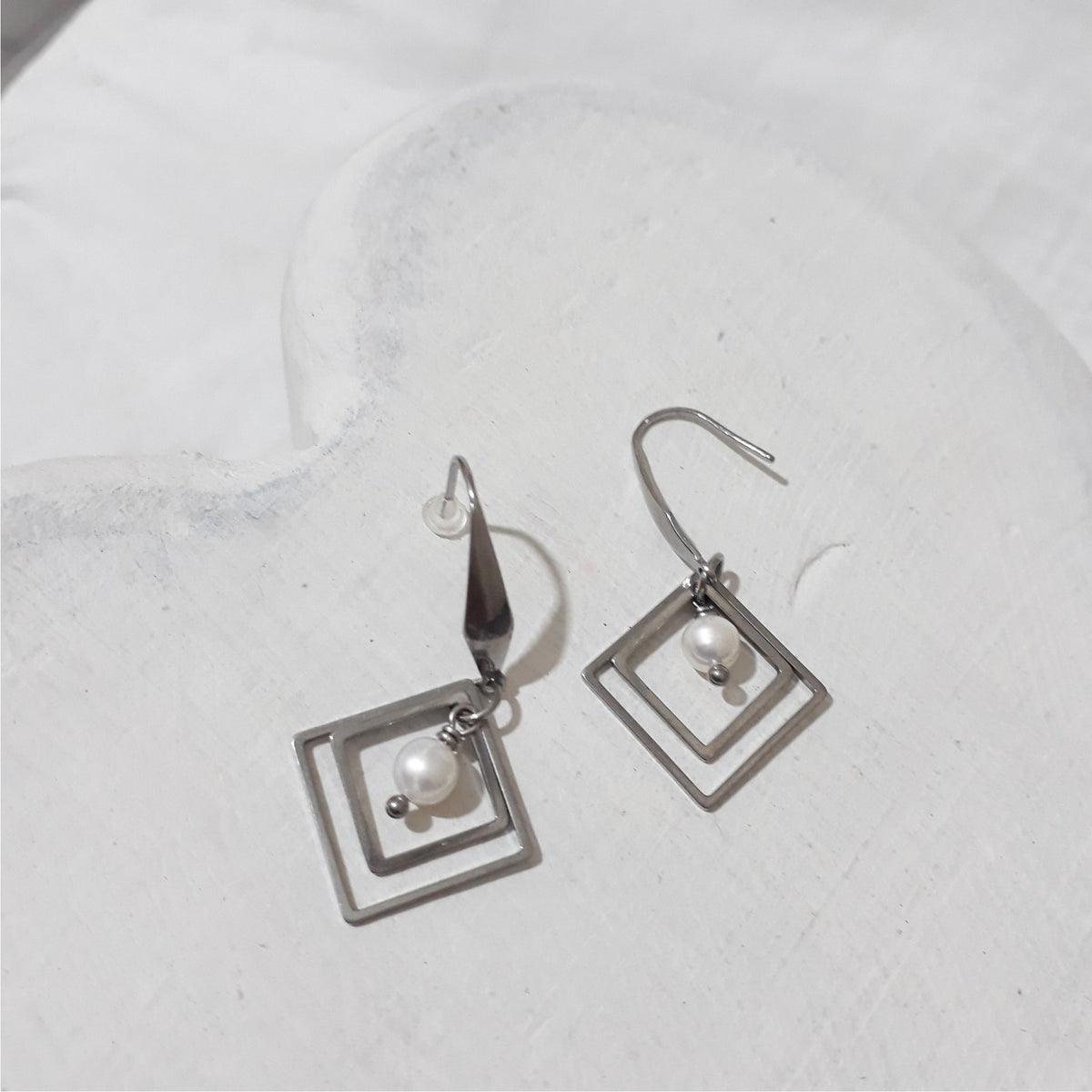 Stainless steel dangle earrings with two nested diamond-shaped frames and a round white freshwater pearl inside each, on elegant hooks.