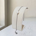 A delicate silver chain bracelet with a single white pearl, displayed on a cream-colored jewelry stand.