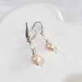 Soft pink pear-shaped freshwater pearls beneath small white rice pearls on silver-tone elegant ear hooks.