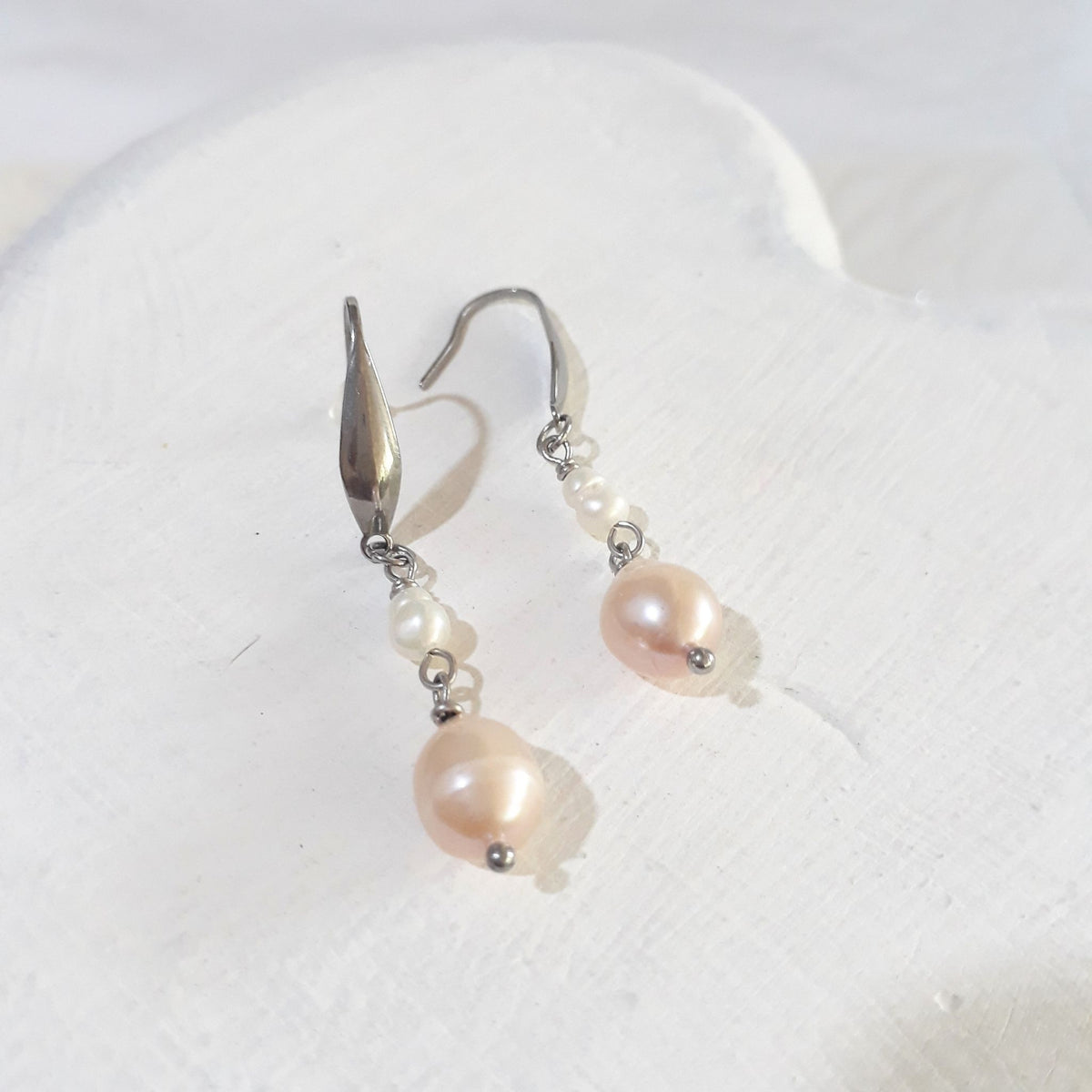 Soft pink pear-shaped freshwater pearls beneath small white rice pearls on silver-tone elegant ear hooks.
