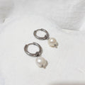 Small silver-tone stainless steel hoop earrings with white button-shaped freshwater pearl charms.