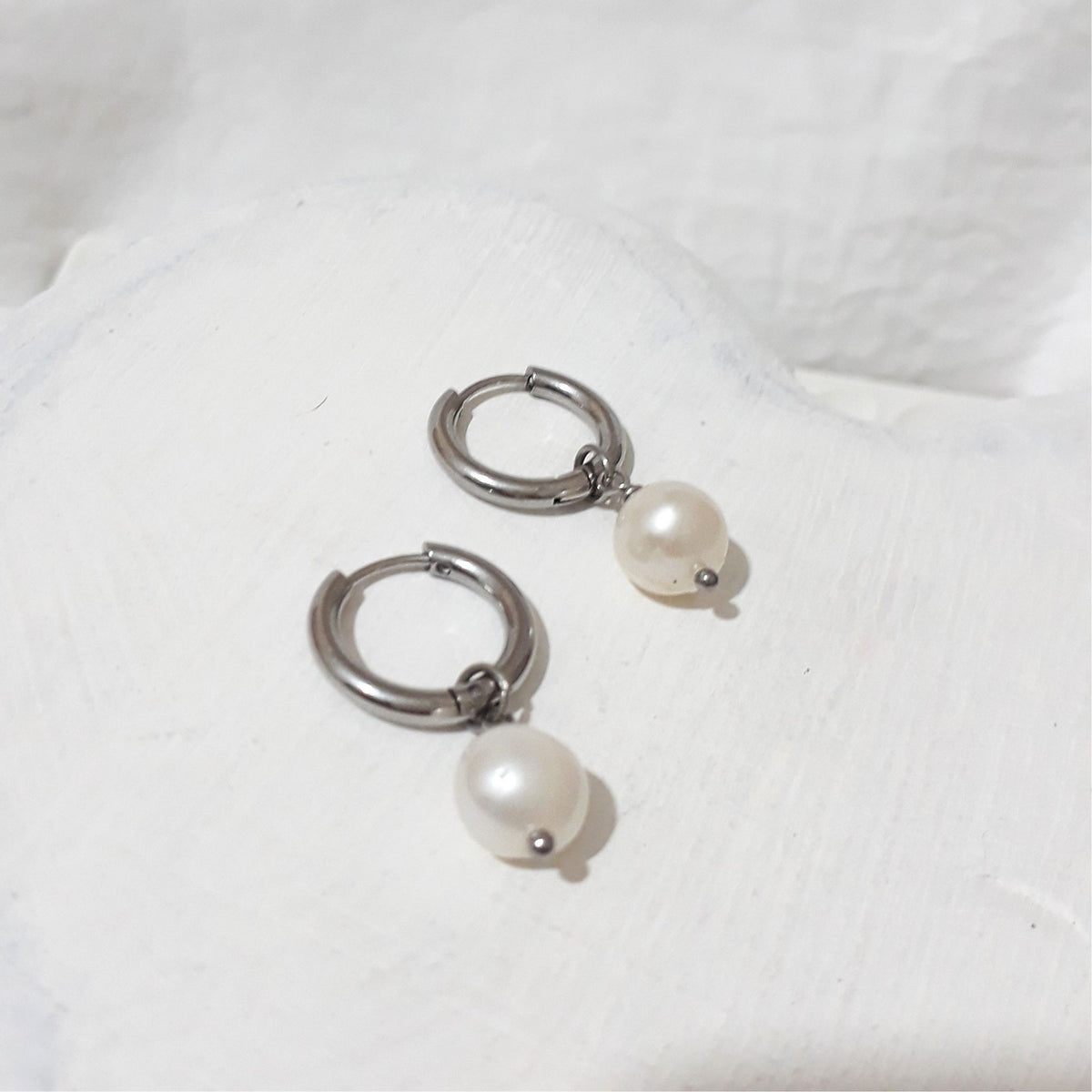 Small silver-tone stainless steel hoop earrings with white button-shaped freshwater pearl charms.