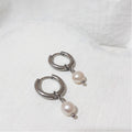 Small silver-tone stainless steel hoop earrings with near-round white freshwater pearl charms hanging beneath each hoop.