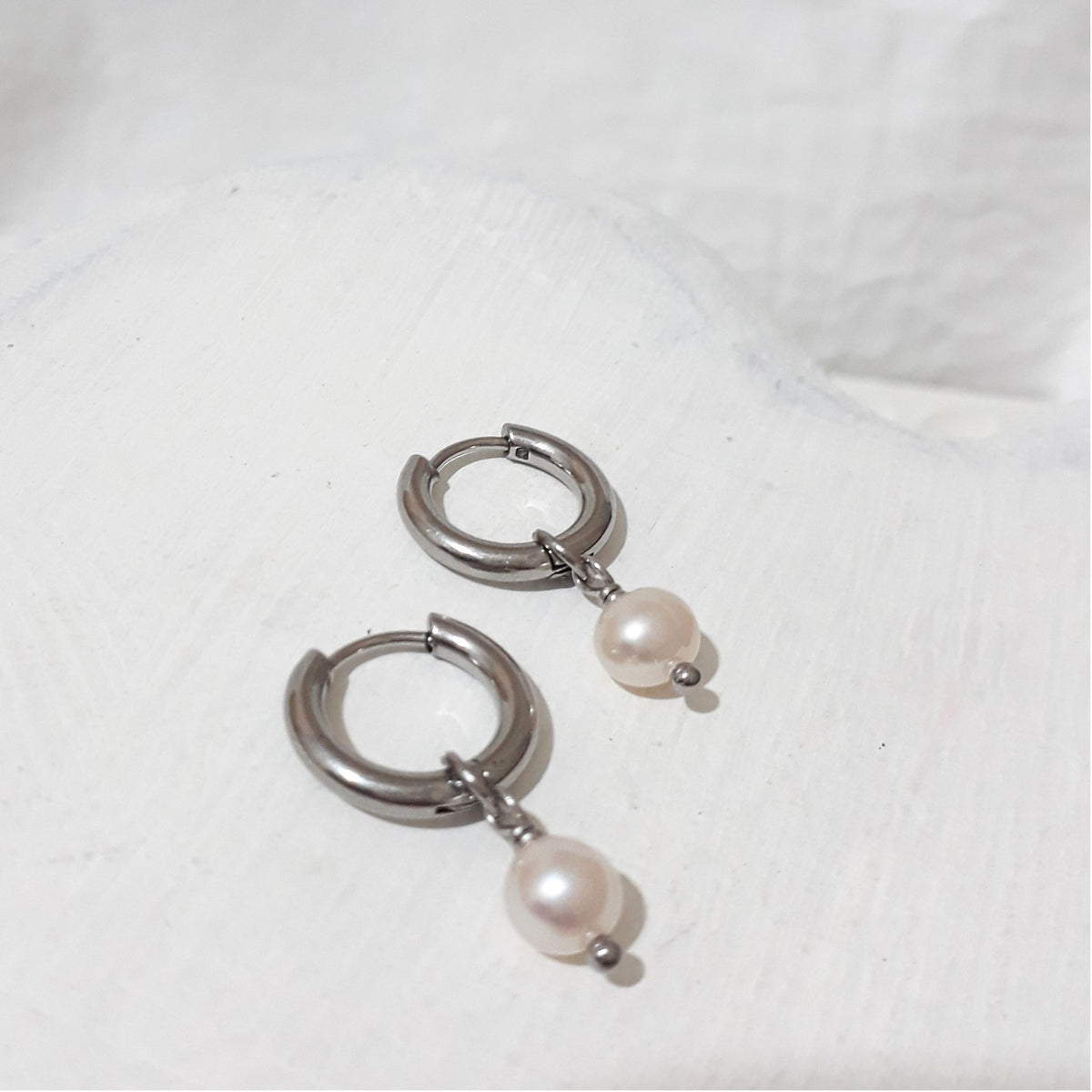 Small silver-tone stainless steel hoop earrings with near-round white freshwater pearl charms hanging beneath each hoop.