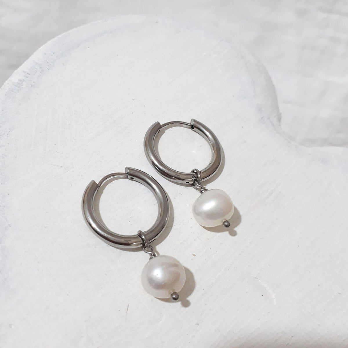 Silver-tone stainless steel hoop earrings with white button-shaped freshwater pearl charms suspended beneath each hoop.