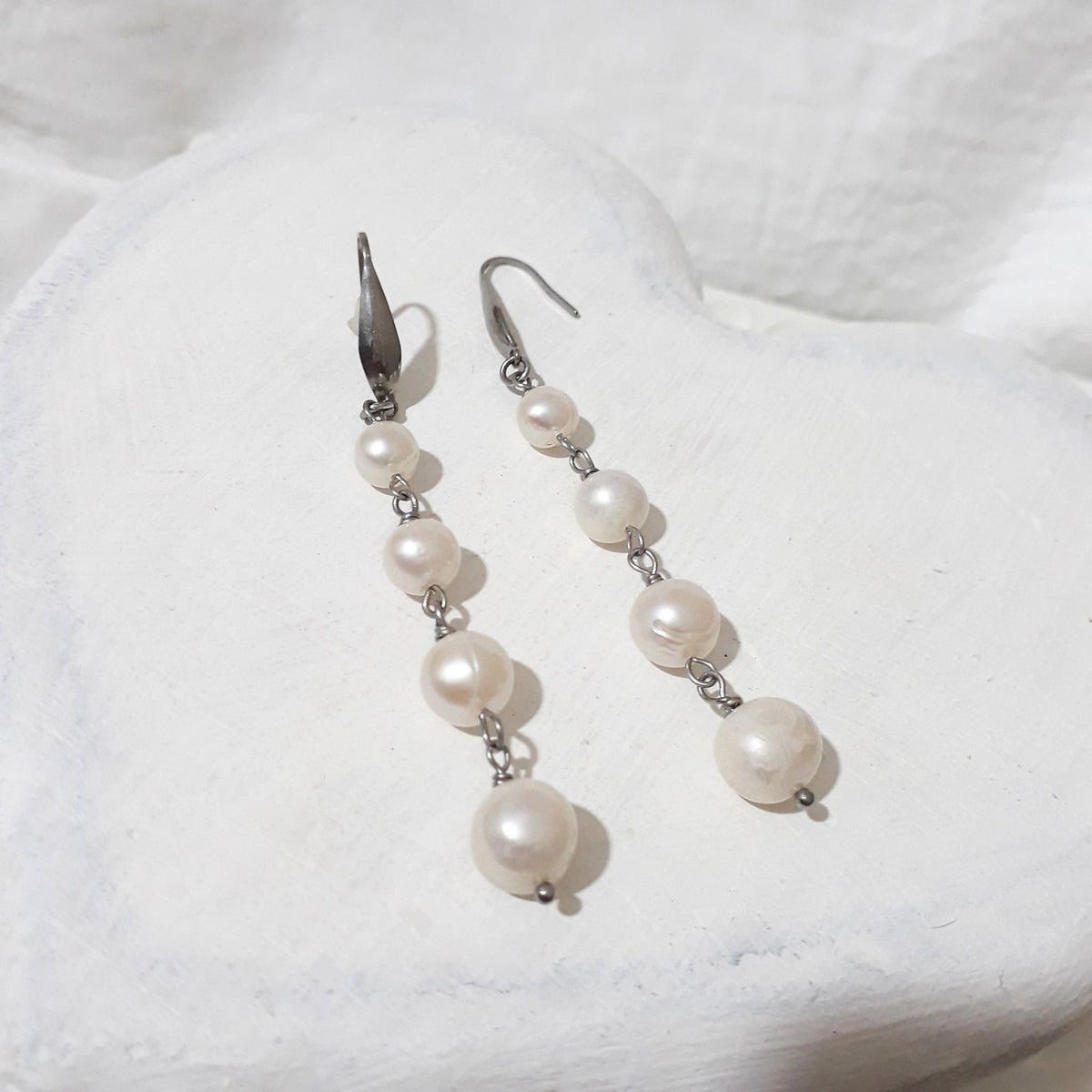 White freshwater pearl cascade earrings with four graduated pearls linked beneath silver-tone elegant ear hooks.