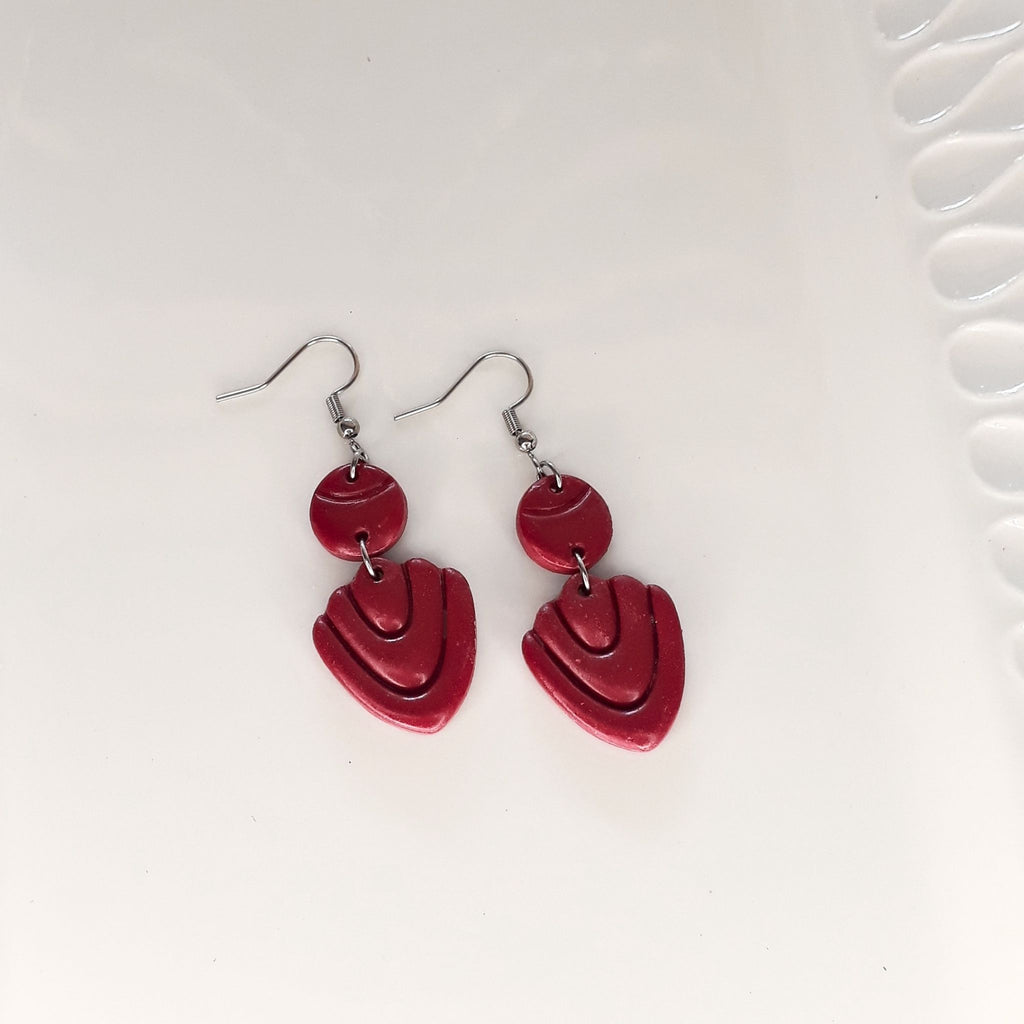 A pair of dark maroon-purple polymer clay drop earrings hanging from silver fishhook wires on a white background.