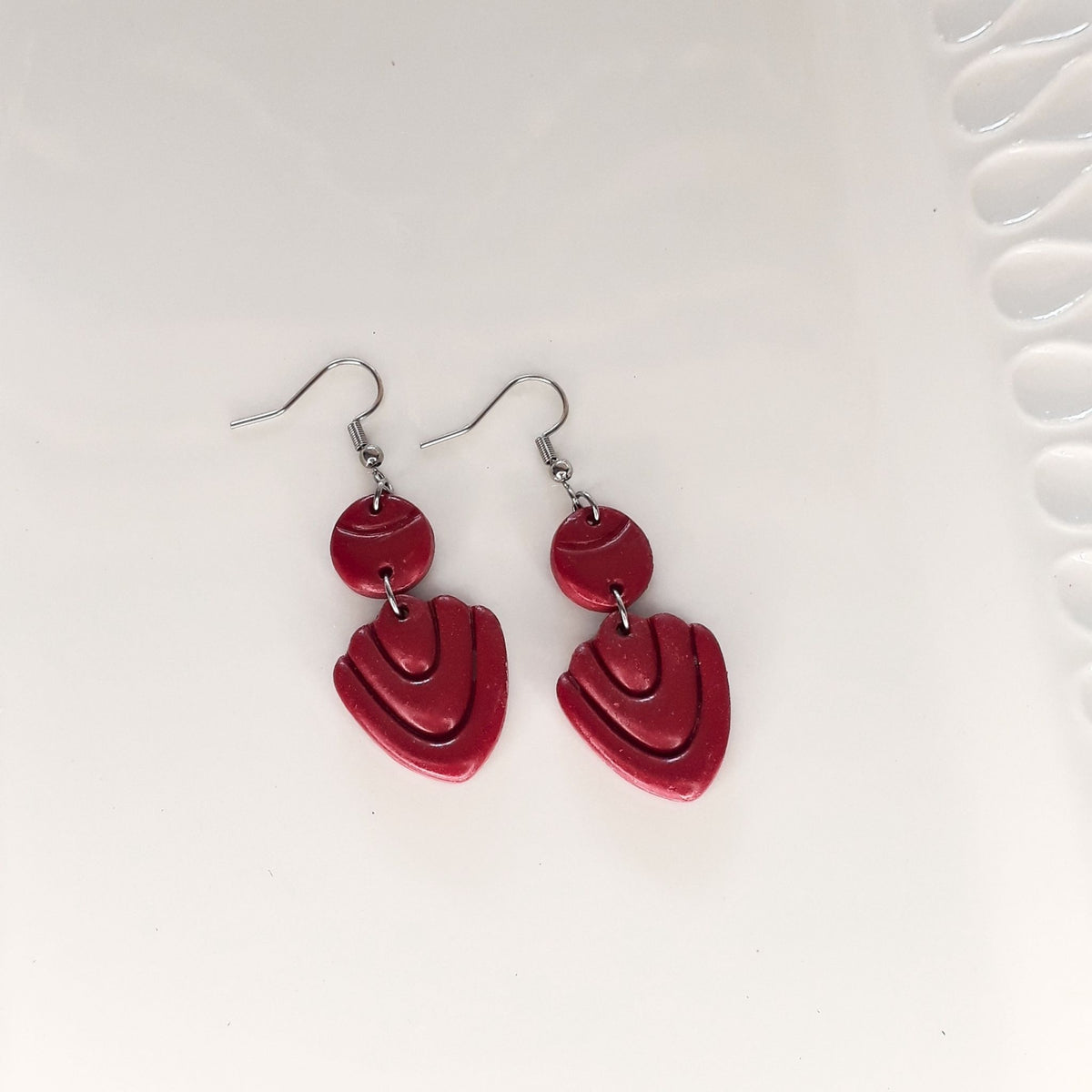 A pair of dark maroon-purple polymer clay drop earrings hanging from silver fishhook wires on a white background.