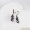 Freshwater pearl drop earrings with three dark charcoal pearls per earring, green and bronze overtones, and silver-tone elegant hooks.