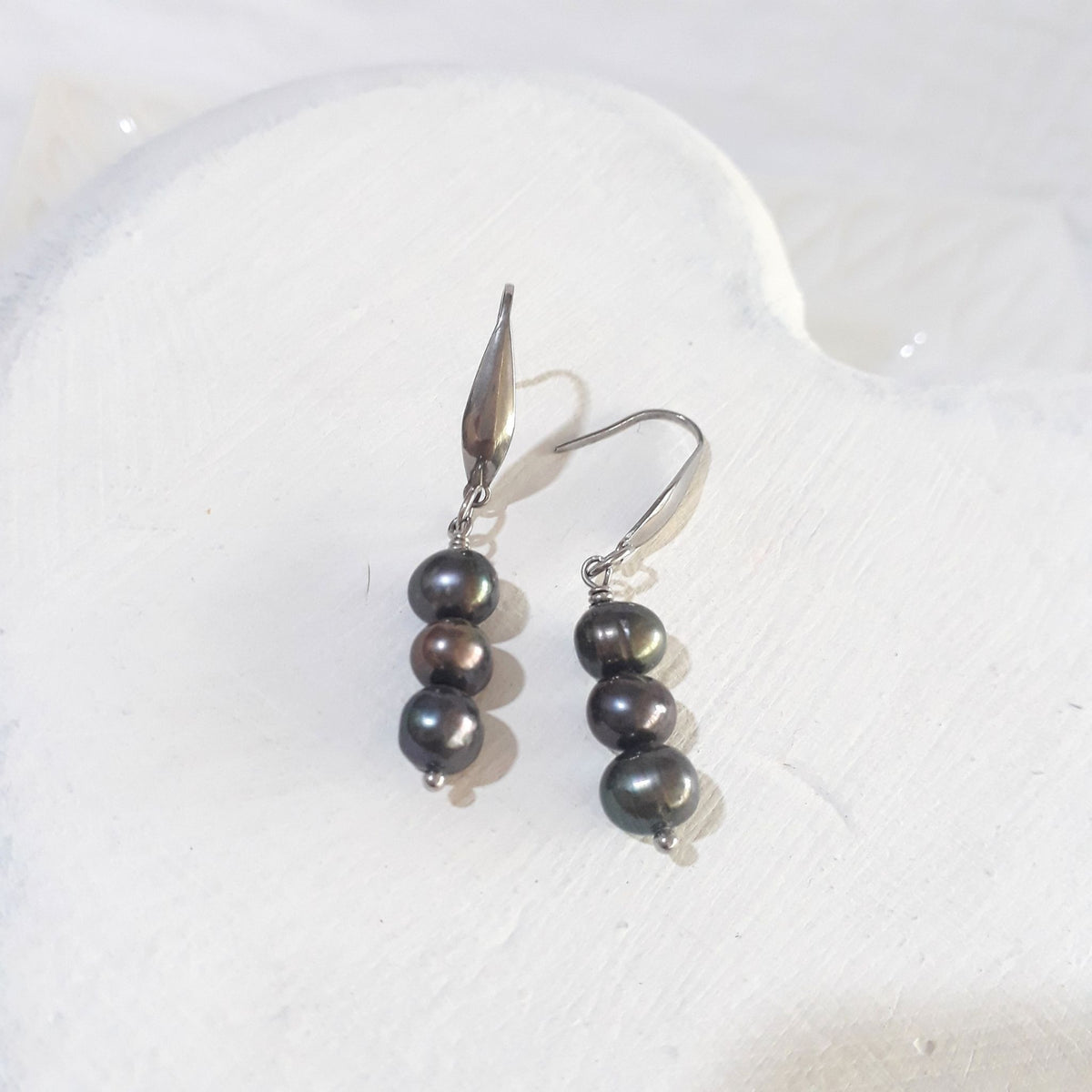 Freshwater pearl drop earrings with three dark charcoal pearls per earring, green and bronze overtones, and silver-tone elegant hooks.