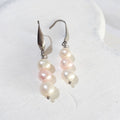 Triple freshwater pearl drop earrings with a pink pearl between two white pearls on silver-tone elegant ear hooks.