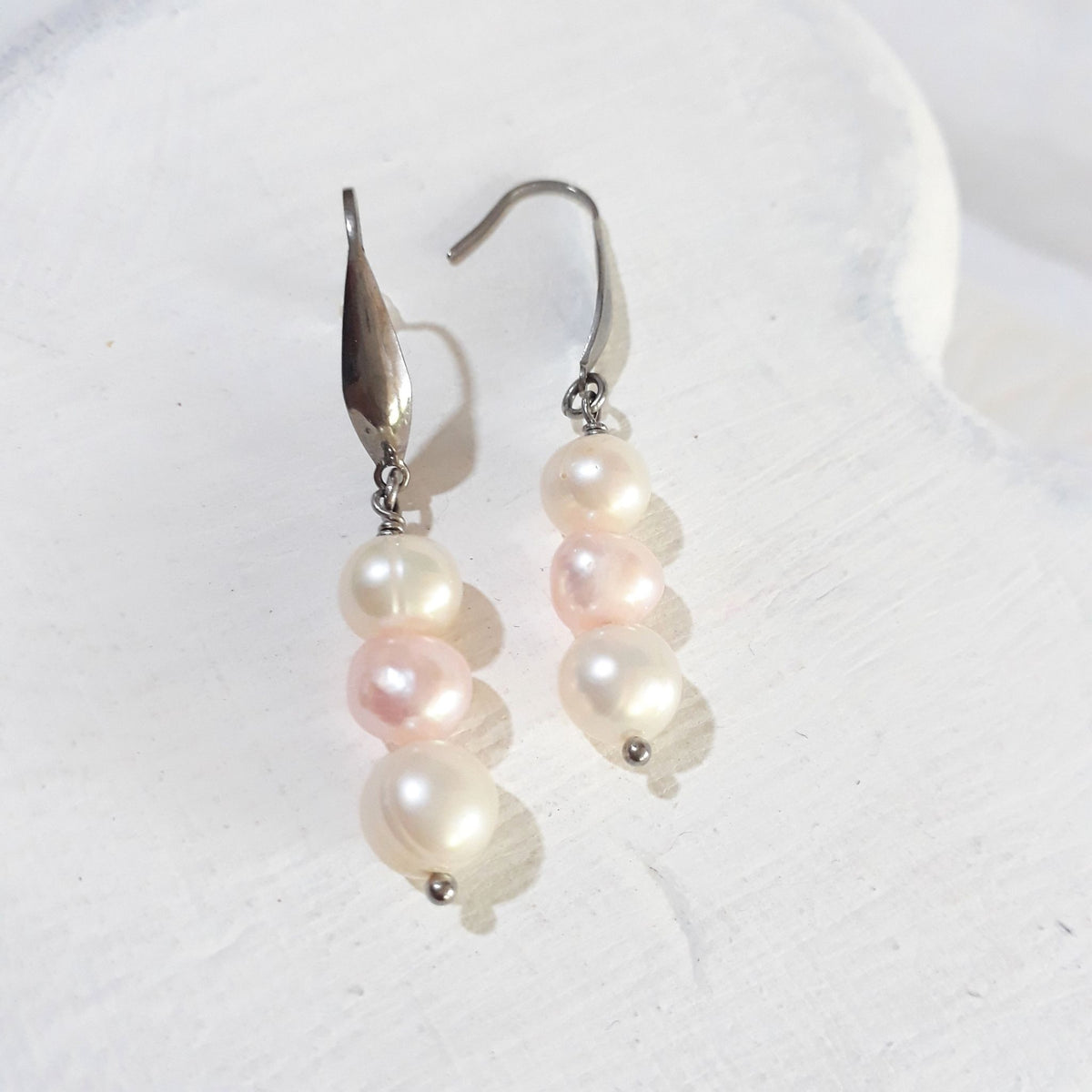 Triple freshwater pearl drop earrings with a pink pearl between two white pearls on silver-tone elegant ear hooks.