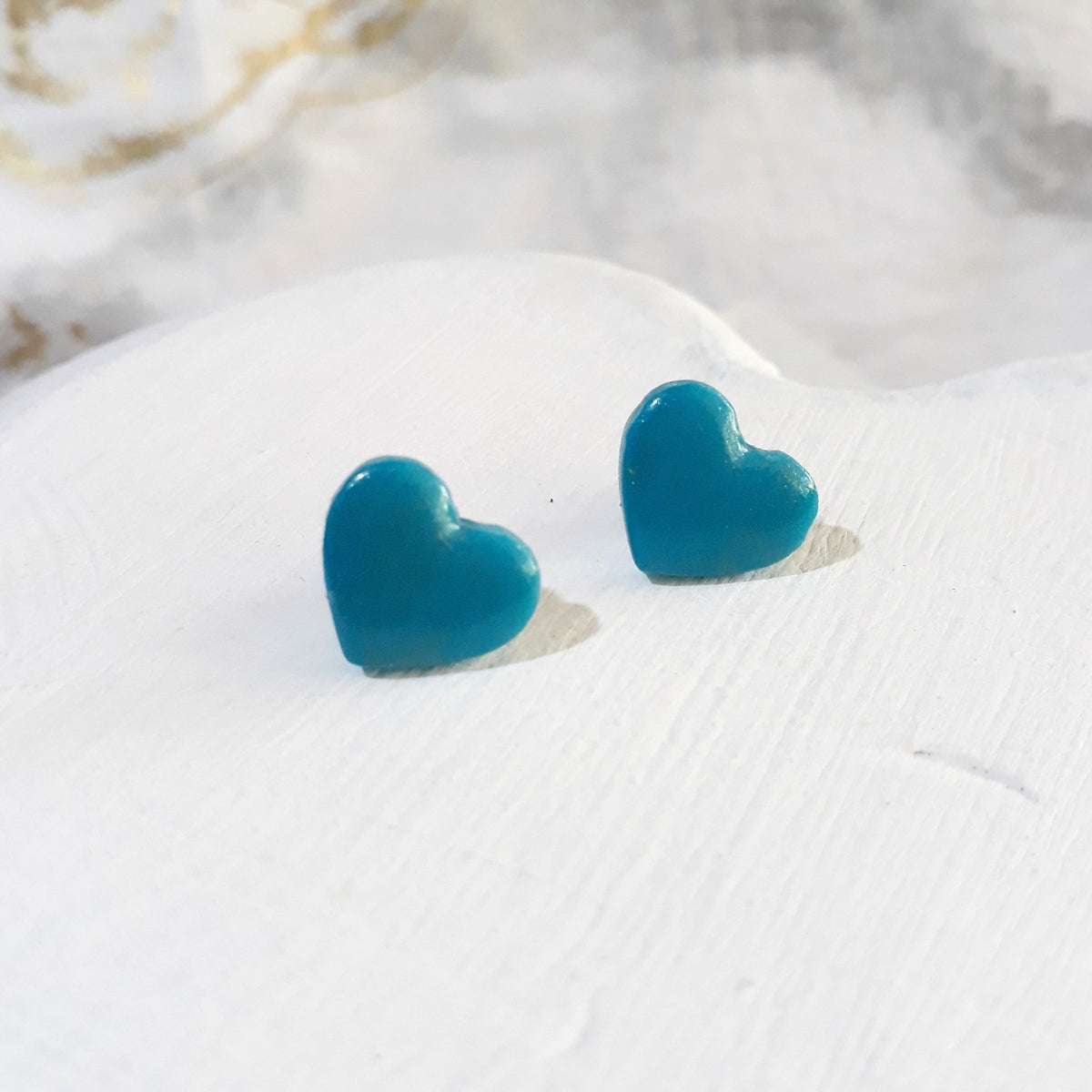 Pair of turquoise heart-shaped polymer clay stud earrings with softly rounded edges and glossy surfaces.