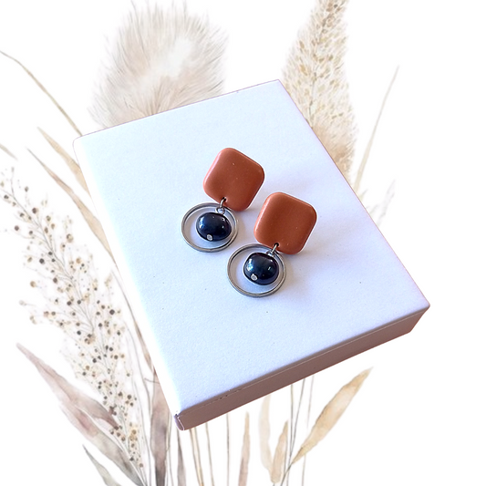 Indulge in the exquisite elegance of our Polymer Clay &amp; Freshwater Pearl Drop Earrings. Handmade with stunning midnight blue freshwater pearls, these earrings feature square tan polymer clay studs with a stainless steel pin.