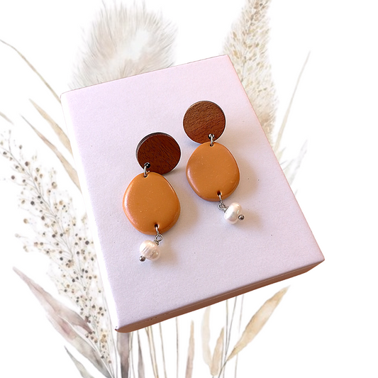 Indulge in the exquisite elegance of our Polymer Clay &amp; Freshwater Pearl Drop Earrings. Handmade with stunning white freshwater pearls, these earrings feature tan polymer clay oval and walnut wood ear studs with a stainless steel pin.